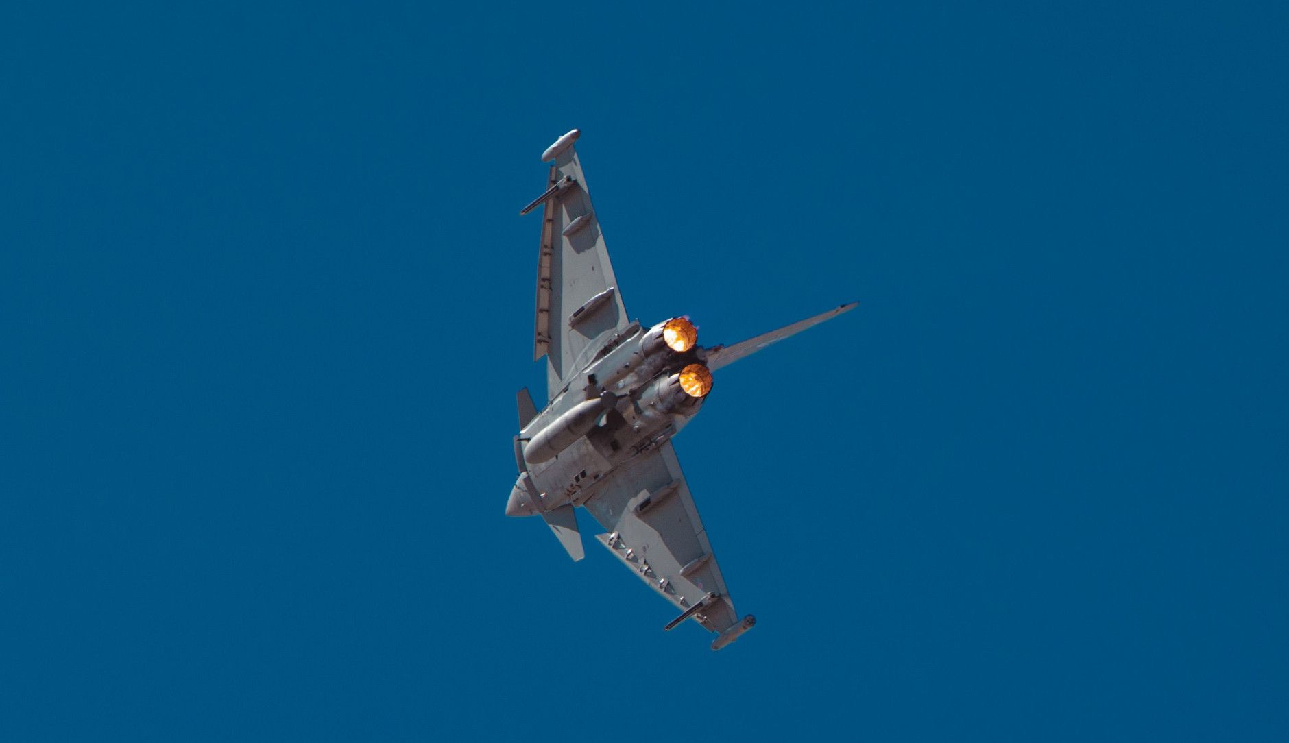 Militärischer Kampfjet fliegt durch blauen Himmel.