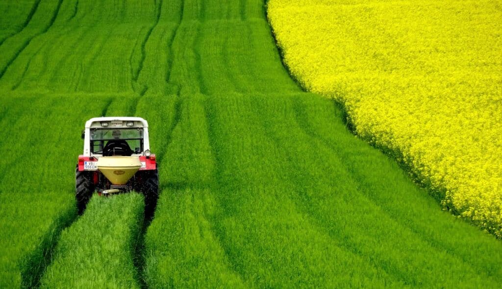 Landwirtschaftlicher Traktor auf grünem Feld mit gelbem Rapsfeld im Hintergrund.
