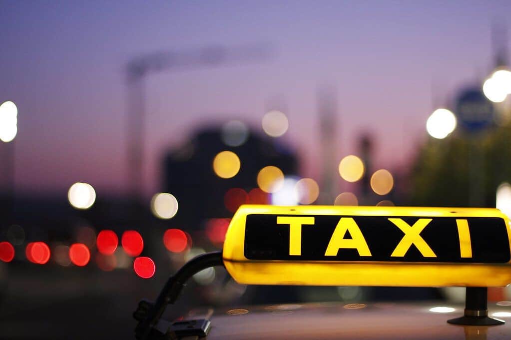 Taxi-Schild bei Nacht mit Stadtlichtern im Hintergrund.