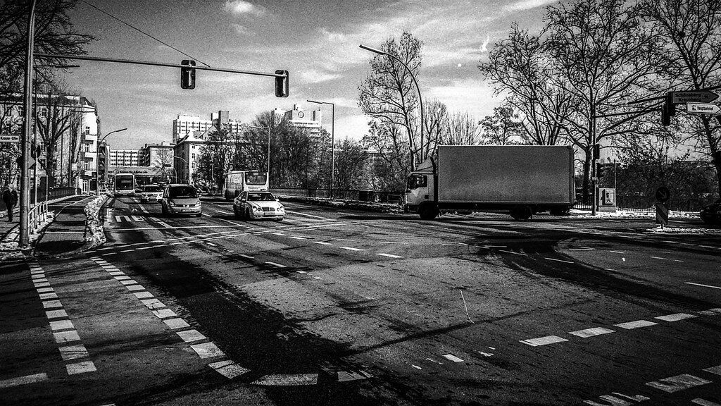 Leere Straße mit Autos und LKWs bei Tag, Bäume und Gebäude im Hintergrund.