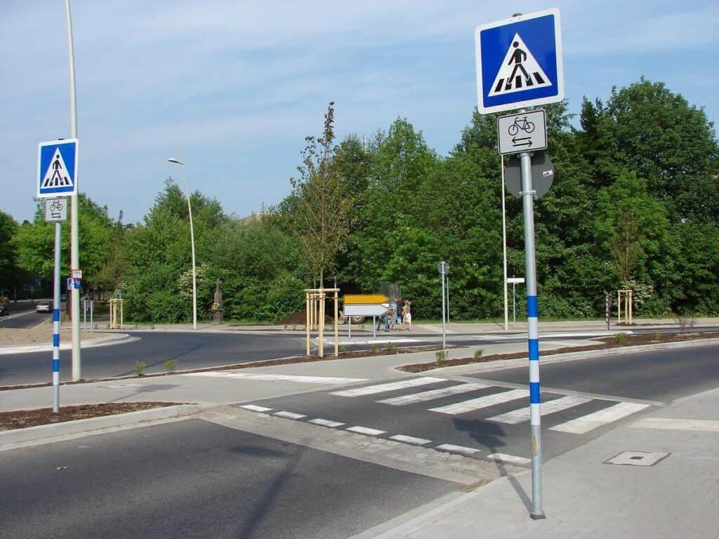 Fußgängerüberweg mit Fahrradweg in Köln, grüne Bäume im Hintergrund.
