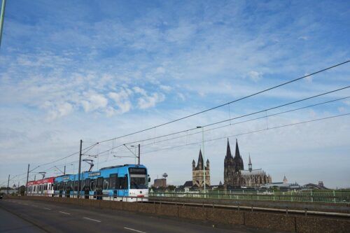 Moderne Stadtbahn fährt an Kölner Dom und Kirche vorbei.