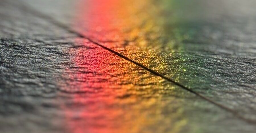 Bunter Regenbogenreflex auf dunkler Holzoberfläche, symbolisch für Vielfalt.