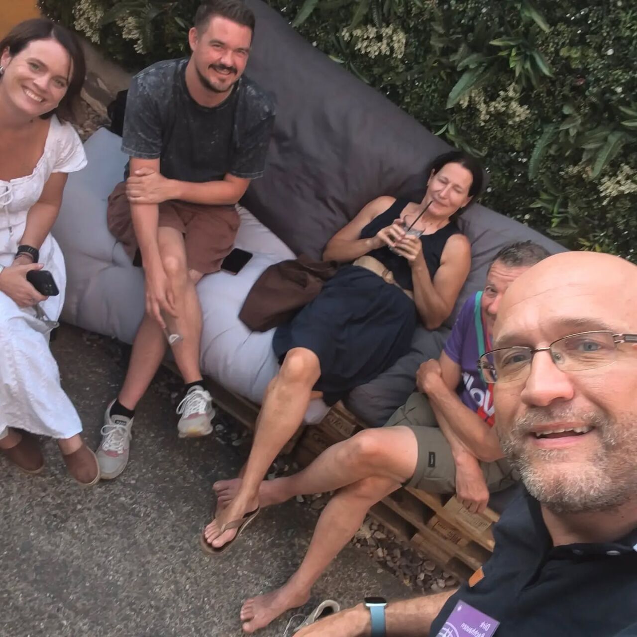 Fünf Personen entspannen und lachen im Garten bei einem Treffen.