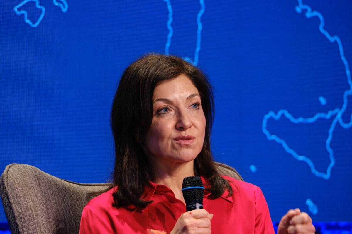 Frau spricht bei einer Pressekonferenz vor einer Weltkarte im Hintergrund.