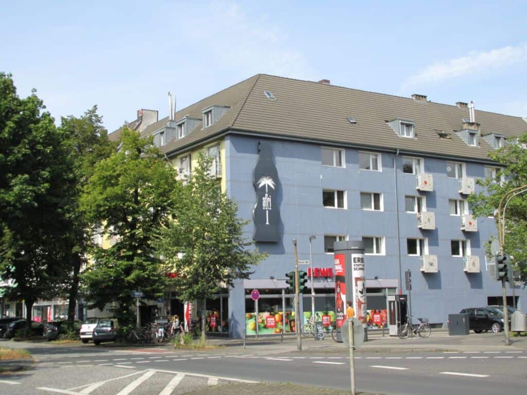 Mehrfamilienhaus in Köln mit Wandkunst und Bäumen im Vordergrund.
