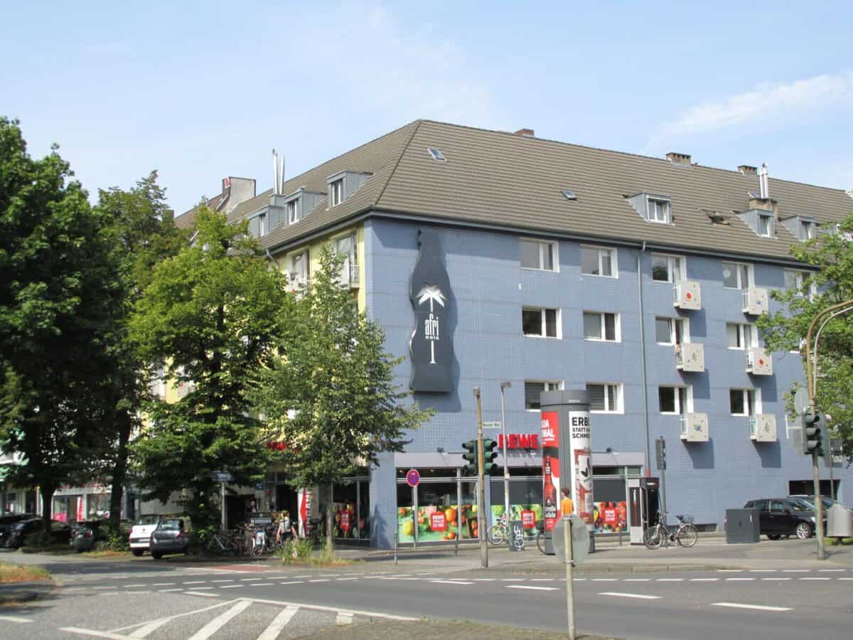 Mehrfamilienhaus in Köln mit Wandkunst und Bäumen im Vordergrund.