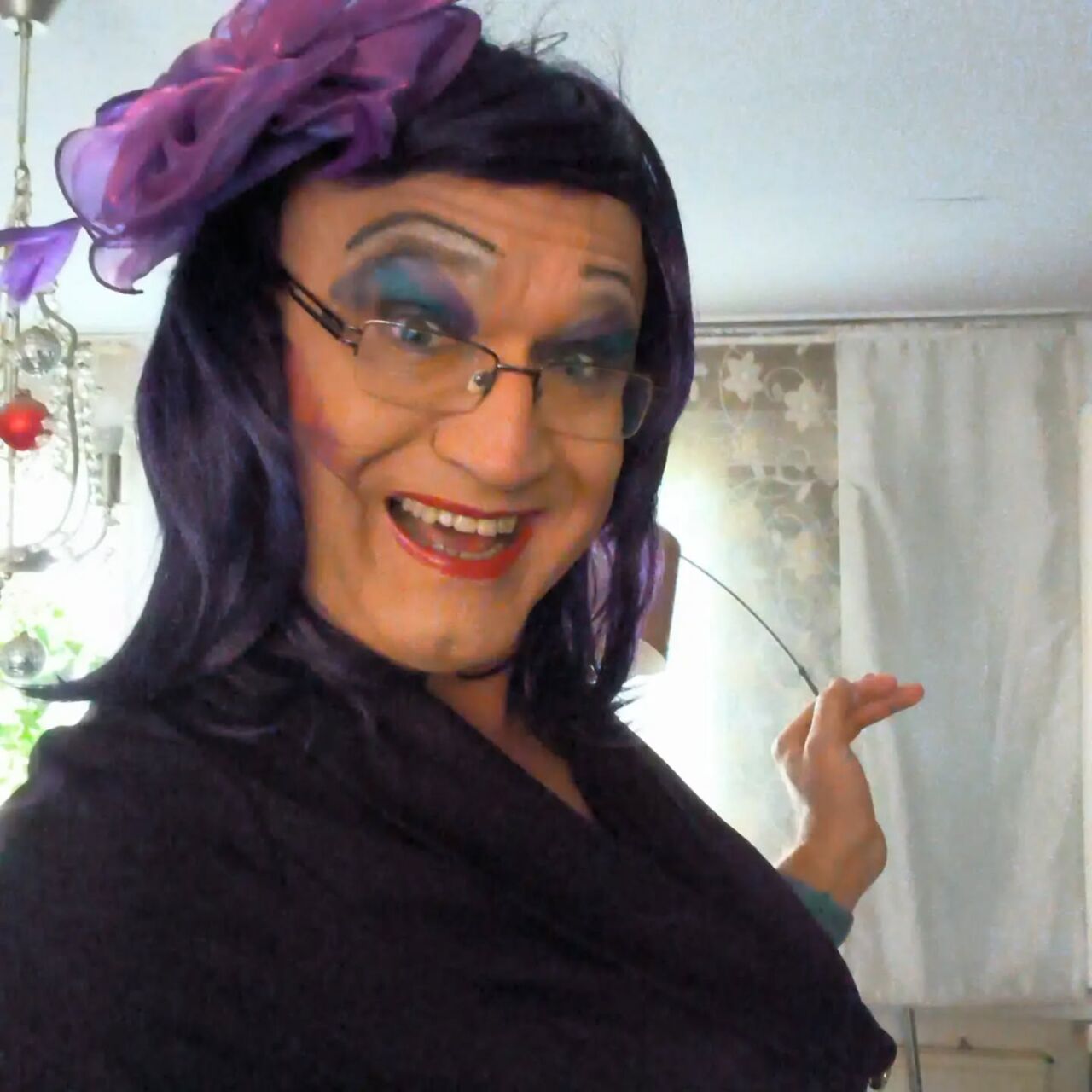 Person in farbenfrohem Drag-Outfit mit lila Haar und Make-up.