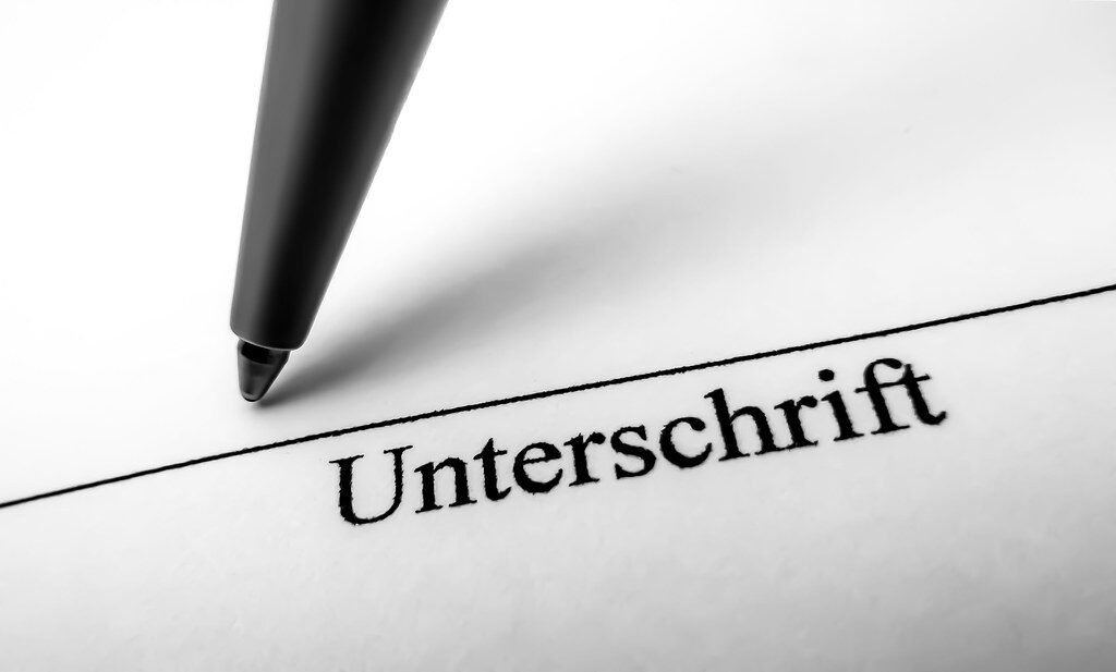 Stift schreibt das Wort 'Unterschrift' auf Papier.