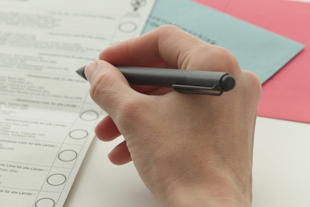 Hand beim Ausfüllen eines Wahlzettels mit Stift.