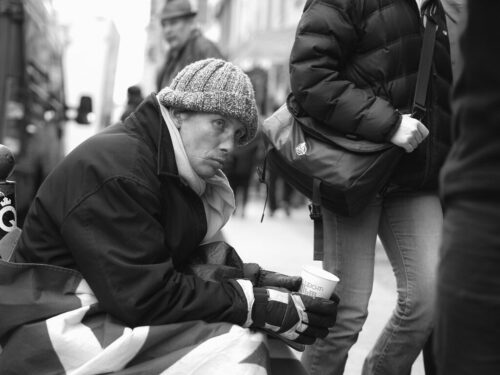 Obdachloser sitzt auf der Straße mit Becher in der Hand in Köln.