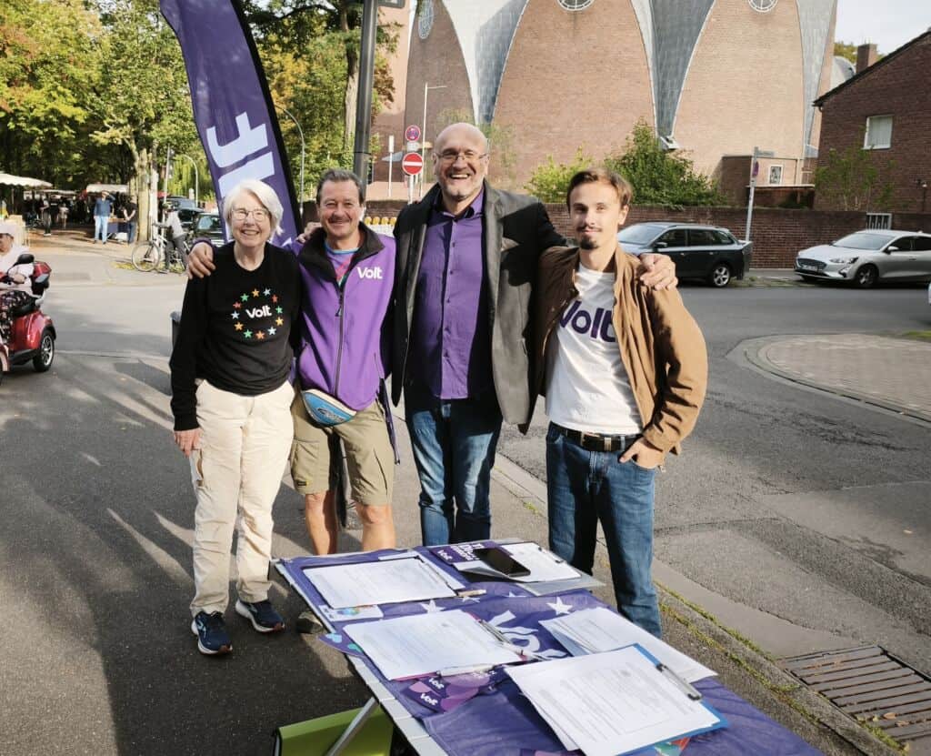 Vier Personen stehen an einem Stand auf dem Wochenmarkt, lächeln und posieren.