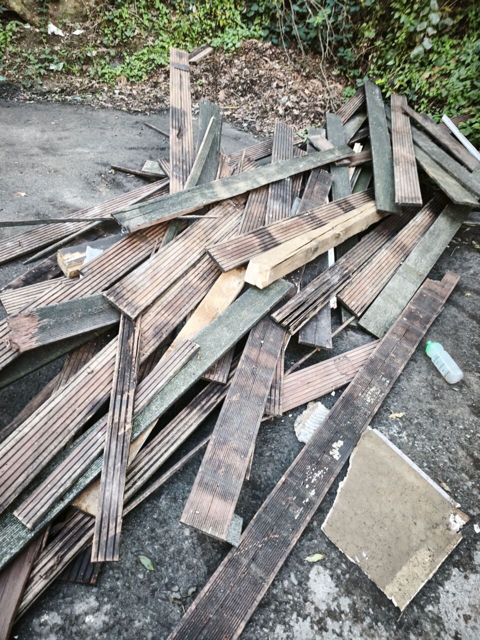 Abfall aus Holz auf Gehweg, Baumaterialien liegen verstreut.