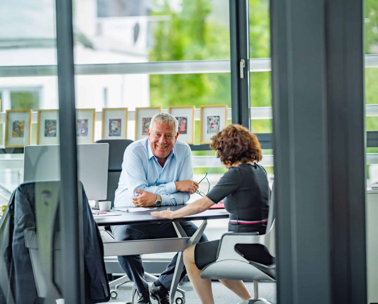 Zwei Personen führen ein Gespräch im hellen Büro mit großen Fenstern und Naturblick.