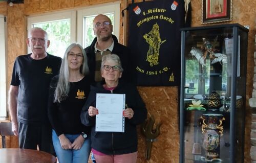 Vier Personen bei Spendenübergabe an die Kölner Mongolenhorde, im Hintergrund Banner.