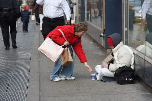 Obdachlose Person erhält Essen von Passantin auf der Straße.