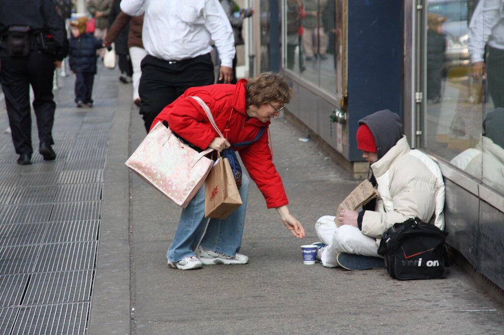 Obdachlose Person erhält Essen von Passantin auf der Straße.