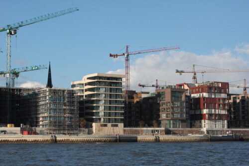 Moderne Wohngebäude im Bau in Köln mit Kranen und Wasser im Vordergrund.