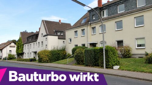 Mehrfamilienhäuser in Merkenich, Köln, mit gepflegtem Garten und Bushaltestelle.