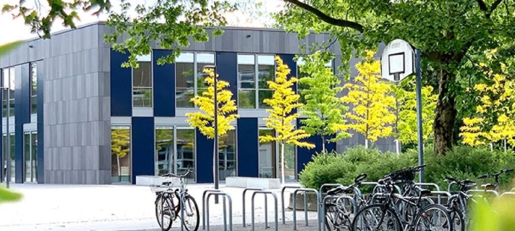 Modernes Schulgebäude mit Fahrradständern und Basketballkorb im Freien.