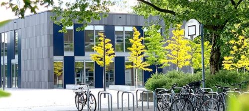 Modernes Schulgebäude mit Fahrradständern und Basketballkorb im Freien.